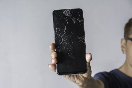 Woman holding a broken touch screen of smart phone on grey background.の写真素材
