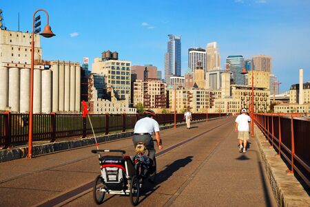 An adult man has special cargo in tow as he crosses the Stone Arch Bridge in Minneapolisのeditorial素材