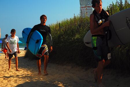 Two young men bring their surfboards back after a satisfying time on the ocean in Montaukのeditorial素材