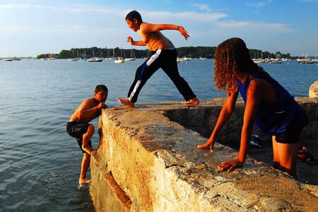 Young friends use a seawall as their launching point on a hot summer afternoonのeditorial素材