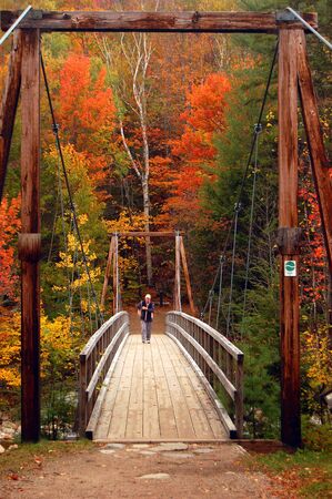 An active senior walks across a pedestrian suspension bridge to view the fall colors of New Hampshire's White Mountainsのeditorial素材
