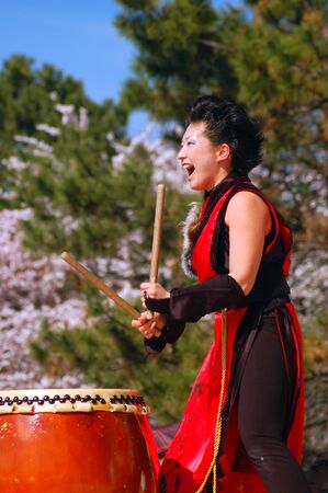 A young woman enthusiastically demonstrates the ancient art of Japanese Taiko drummingのeditorial素材