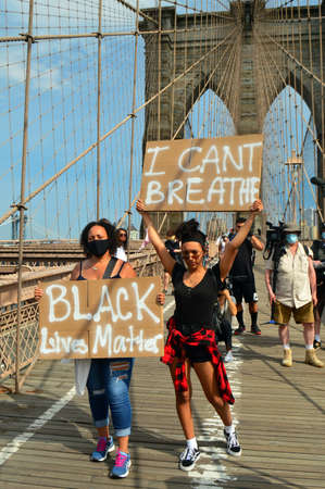 Two adult women hold up signs protesting police brutality as they march across the Brooklyn Bridgeのeditorial素材