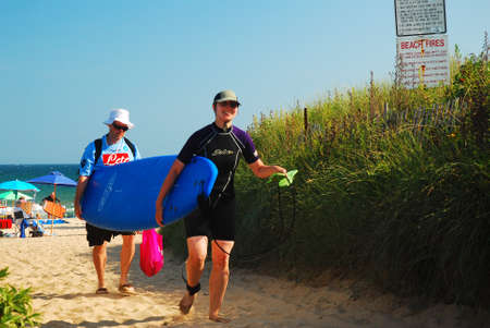 A couple carries their surfboard back to their car after a productive day on the waves in Ditch Plains Beach, Montauk, New Yorkのeditorial素材