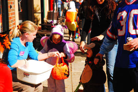 A store employee hands out treats to costumed trick or treaters in a downtown districtのeditorial素材
