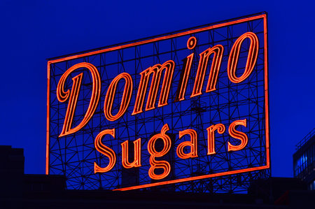 A neon Domino Sugar sign glows against the dusk sky in Baltimore Marylandのeditorial素材