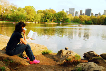 A young woman is more intrigued with her book than the New York Skyline in Central Parkのeditorial素材