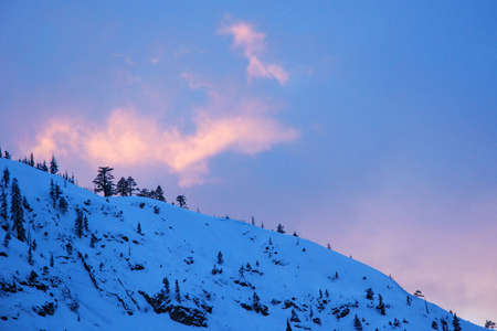The sunset light hits a wispy cloud over a snowy mountainの写真素材