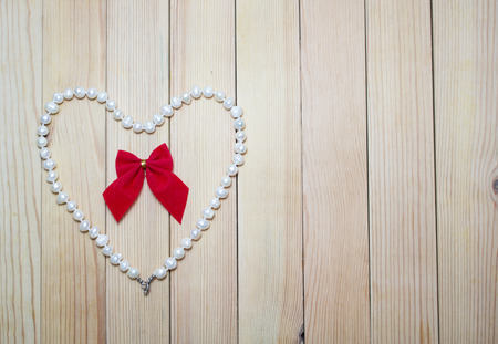 Pearl necklace with red bow in a heart on a wooden board. Love. Valentine's Dayの写真素材