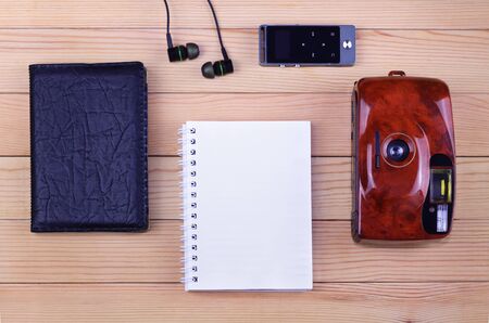 Top view: Blank notepad with old photo camera, black passport, earphones and mp3 player on a wooden table. Travel conceptの写真素材