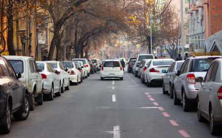 View of a city autumn street with parked cars on both sides, with buildings and trees in the backdropの写真素材
