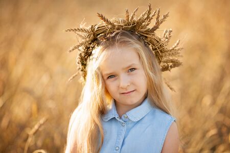 A little blonde girl is standing in a wheat field in summer and a wreath on her head.の写真素材