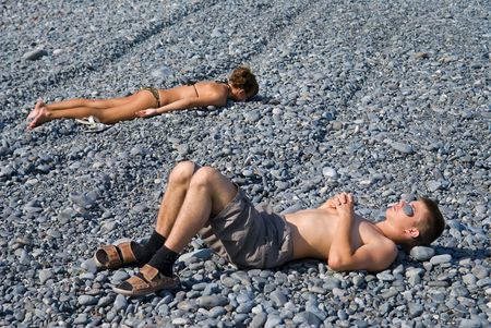 The boy and girl suburn on beach with grey-blue pebbles. Early evening.の写真素材
