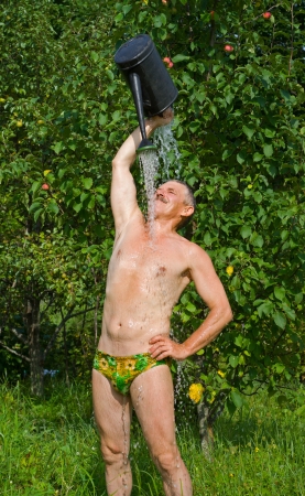 The man waters himself from a watering can in orchard.の写真素材