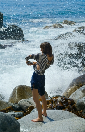 The young woman in wet old striped vest on stones at surf.の写真素材
