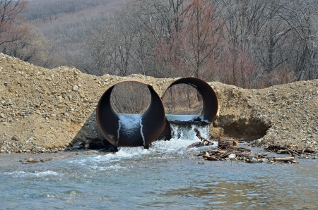 An earth dam with two pipes and flowing water.の写真素材