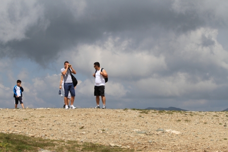 Several people are on top of the mountain against the dark clouds. One of them looks through binoculars.のeditorial素材