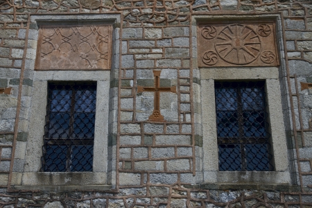 Two wooden windows and a cross on an old stone wall of a building の写真素材