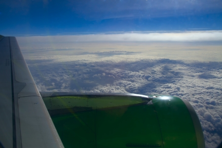 Aircraft wing on a background of clouds from the window. Blue sky, white clouds and city below.