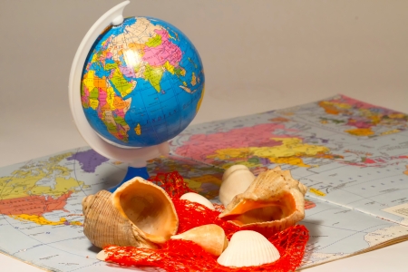 Seashells and small globe on a book with a geographical map 