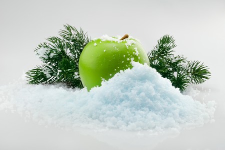 Green delicious Christmas apple in snow with christmas tree branches on the backgroundの写真素材