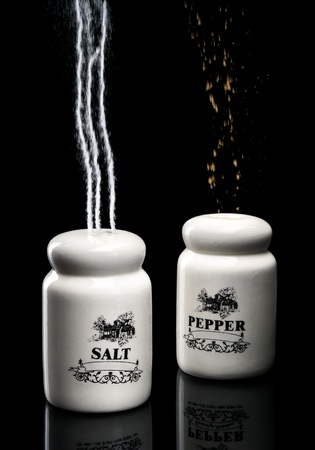 Salt an pepper shakers pouring up over black backgroundの写真素材