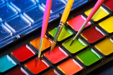 Closeup of a palette of watercolor paints with three brushes
