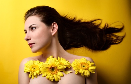 Topless portrait of a beautiful young woman covered with yellow flowers isolated on yellow backgroundの写真素材