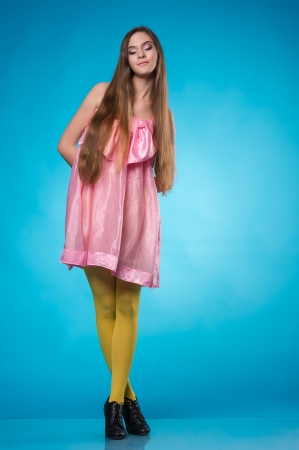 Young teen girl in a pink dress posing with closed eyes over blue backgroundの写真素材