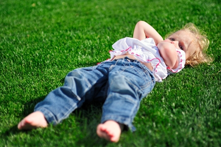 Cute little girl laying on the green grass in the parkの写真素材