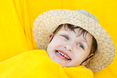 Girl after swimming wrapped in a yellow towel, lies and smilesの写真素材
