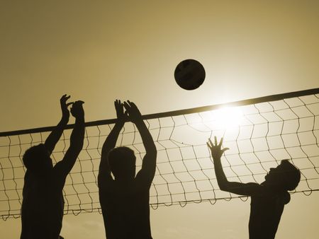 Silhouettes of three men playing beach volleyball, の写真素材