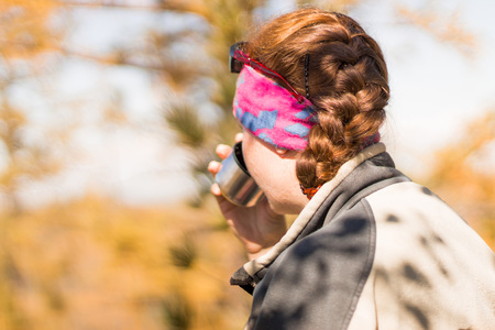 redhead girl drinks tea from a flask in autumn in the mountains, a bandanna on his head, in a jacket.の写真素材
