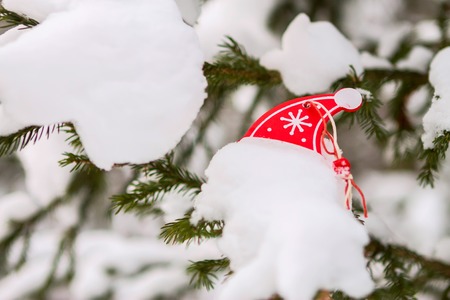 Christmas wooden ornaments toy cap with ribbon hanging on a Christmas tree with snow.