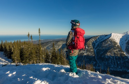 Freerider girl is standing on the mountainside in a helmet and with a backpack and looks into the...