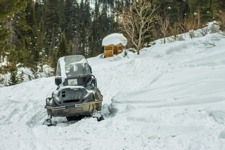 Snowmobile on the hillside against the backdrop of a wooden house in the woods.の写真素材
