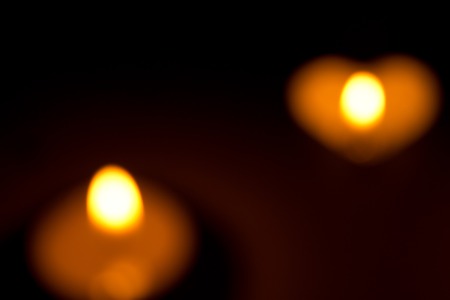Small round candle with heart-shaped tablet is lit in the dark.の写真素材