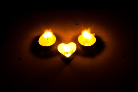 Small round candle with heart-shaped tablet is lit in the dark.の写真素材