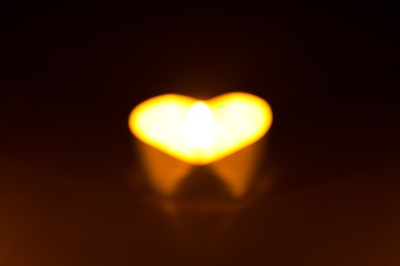 Small round candle with heart-shaped tablet is lit in the dark.の写真素材