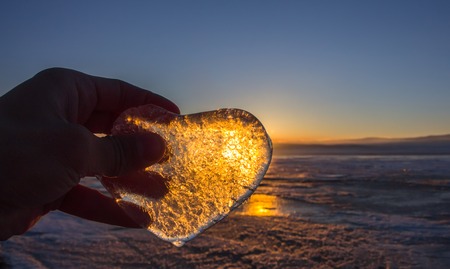 Icy heart in his hand in light of sunset. lake Baikal.の写真素材