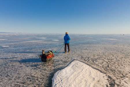 Girl with a sledge and trekking pole is on the ice of Lake Baikal.の写真素材