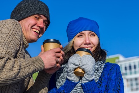 Couple in winter sweater hugging cups of coffeeの写真素材