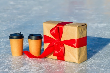 craft gift with red ribbon and cups of coffee on the ice rinkの写真素材
