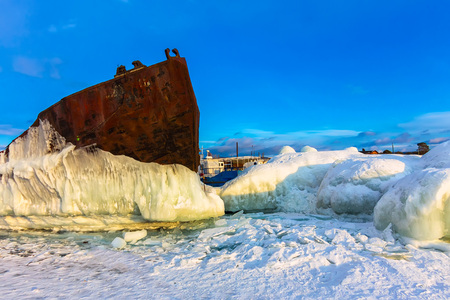 Old rusty ship on ice covered sunset standing on the shore.