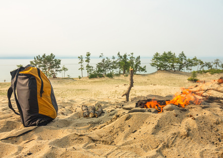 small yellow backpack standing near the bonfire in the sand.の写真素材