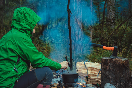 Woman traveler cooking food in kettle on fire in forestの写真素材