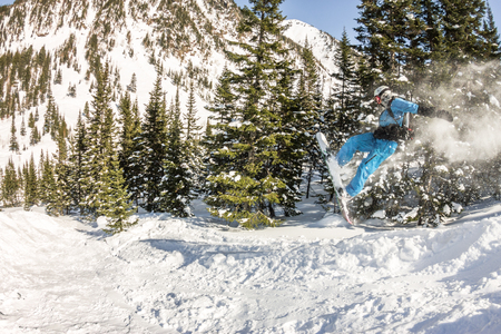 Snowboarder freerider jumping from a snow ramp in the sun on a background of forest and mountains.の写真素材