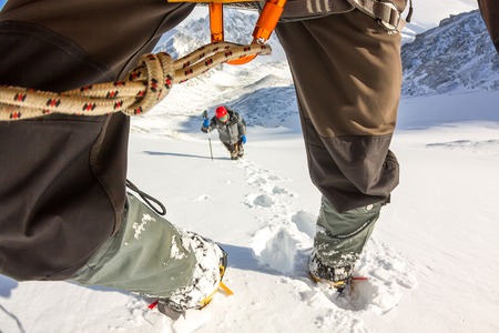 Tied climbers climbing mountain with snow field tied with a rope with ice axes and helmets first person.の写真素材