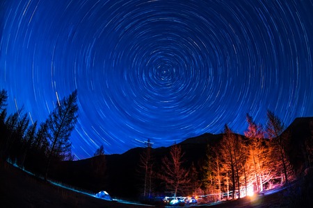 Star Trail in sky above the mountains fire in the tent camp.