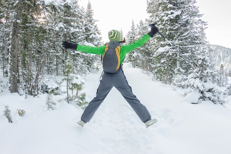 happy tourist girl with a backpack walks in a winter forest among large trees.の写真素材